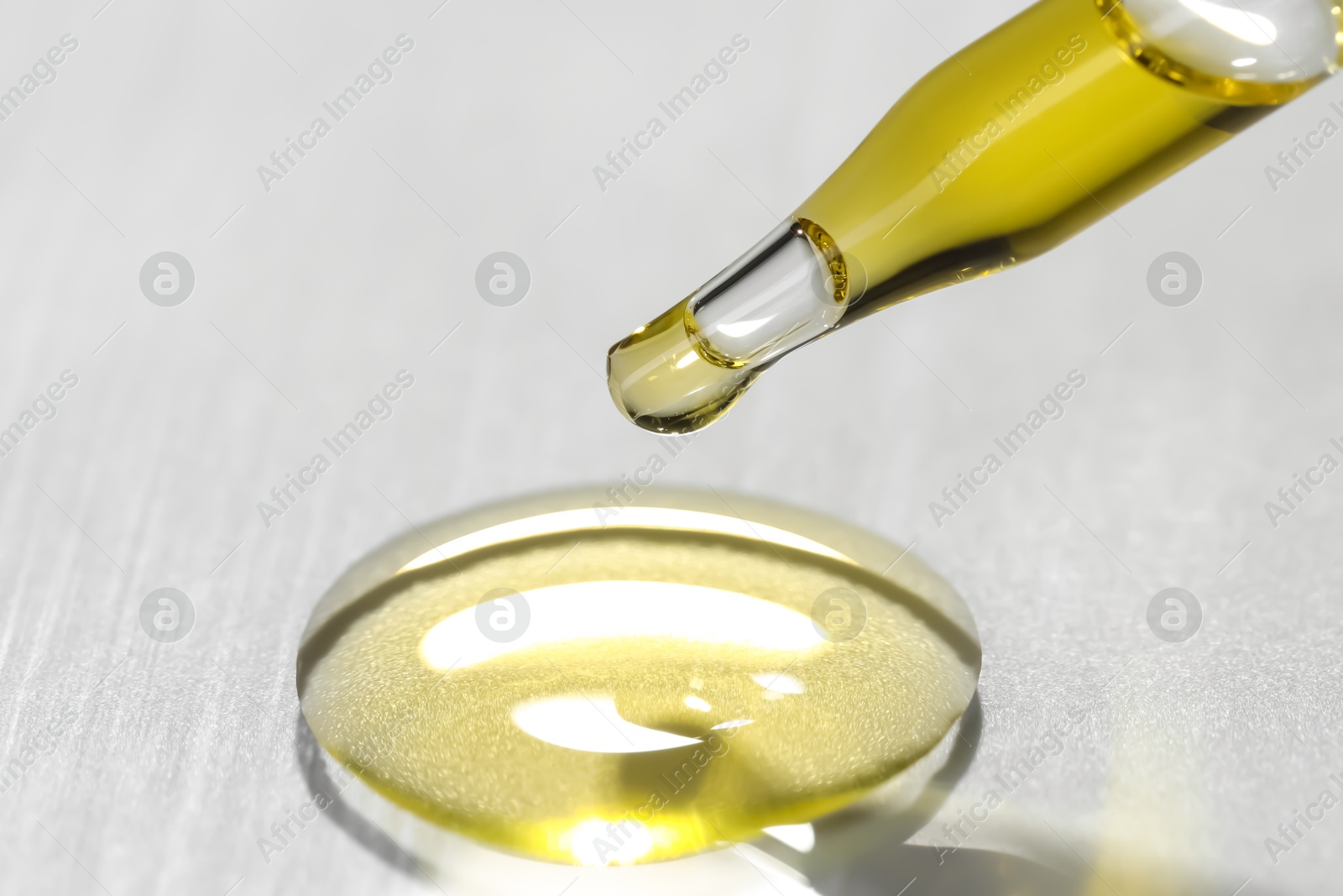 Photo of Cosmetic oil dripping from pipette on light grey background, closeup