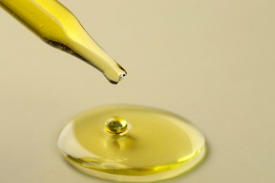 Photo of Cosmetic oil dripping from pipette on dark beige background, closeup. Space for text