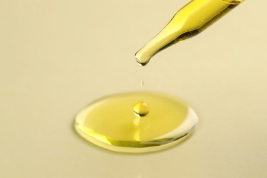 Cosmetic oil dripping from pipette on dark beige background, closeup