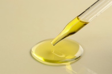 Photo of Cosmetic oil dripping from pipette on dark beige background, closeup. Space for text