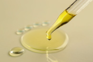 Photo of Cosmetic oil dripping from pipette on dark beige background, closeup. Space for text