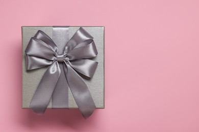 Gift box with bow on dusty pink background, top view