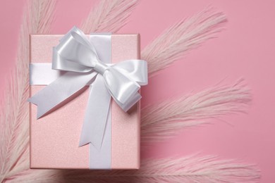 Photo of Gift box with bow and feathers on dusty pink background, top view