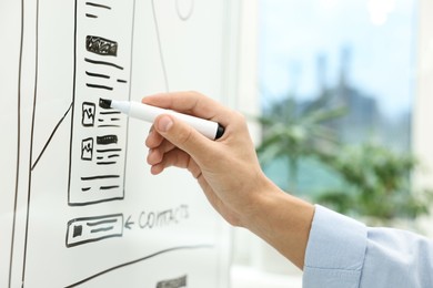 Photo of Developing UI design. Man drawing website wireframe on whiteboard indoors, closeup