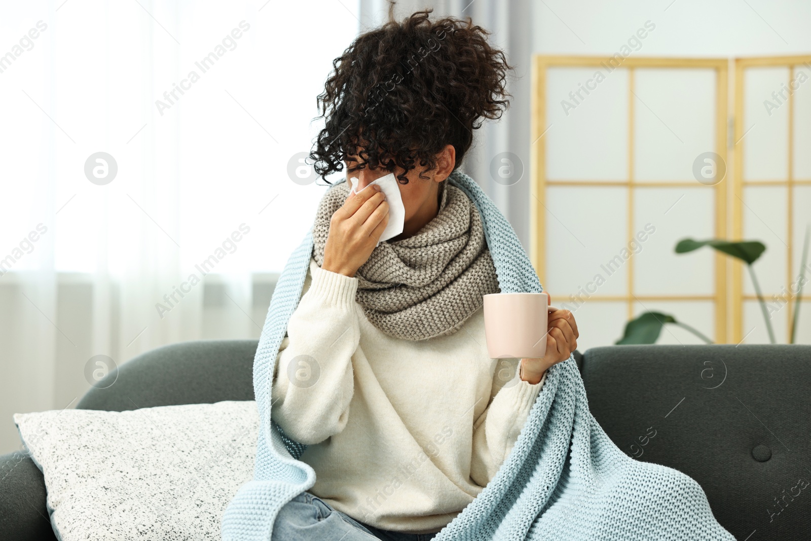 Photo of Cold symptom. Young woman with tissue and cup of hot drink at home