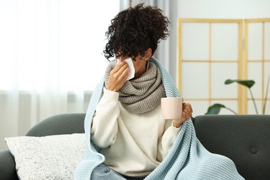 Cold symptom. Young woman with tissue and cup of hot drink at home