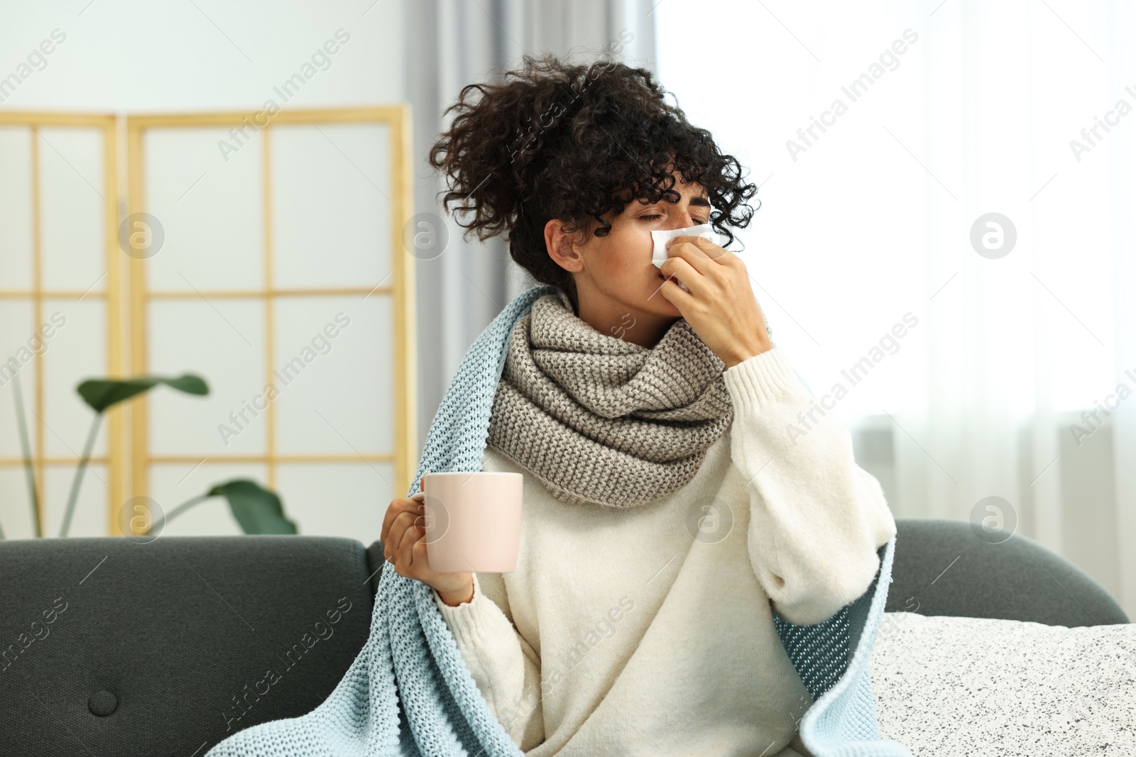 Photo of Cold symptom. Young woman with tissue and cup of hot drink at home