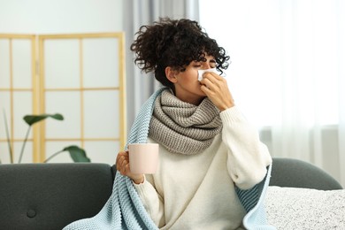 Cold symptom. Young woman with tissue and cup of hot drink at home