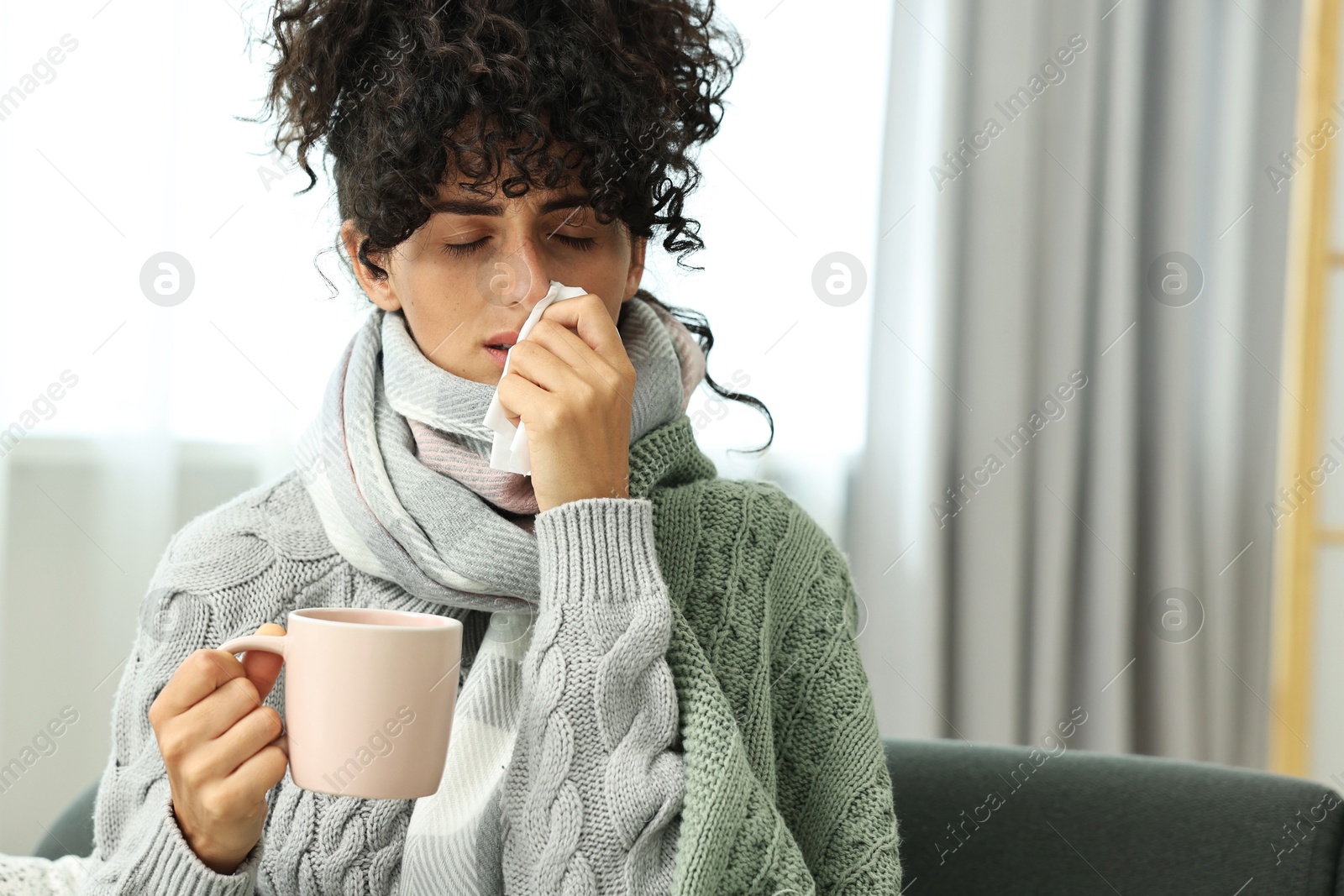 Photo of Cold symptom. Young woman with tissue and cup of hot drink at home, space for text