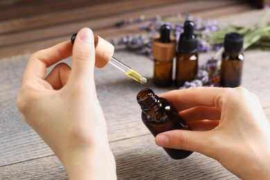 Photo of Woman using essential oil at wooden table, closeup