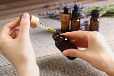 Photo of Woman using essential oil at wooden table, closeup