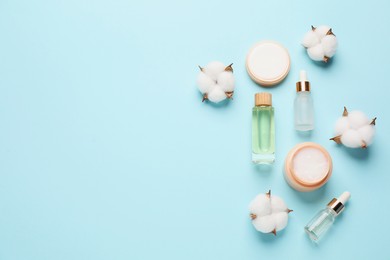 Photo of Different cosmetic products and cotton flowers on light blue background, flat lay. Space for text