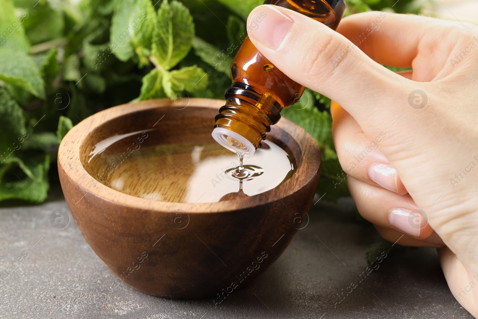 Photo of Woman dripping essential oil into bowl with water at grey table, closeup