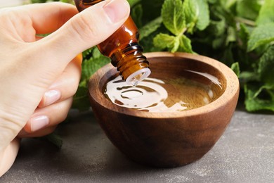 Photo of Woman dripping essential oil into bowl with water at grey table, closeup