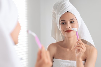 Photo of Beautiful woman shaving face near mirror indoors