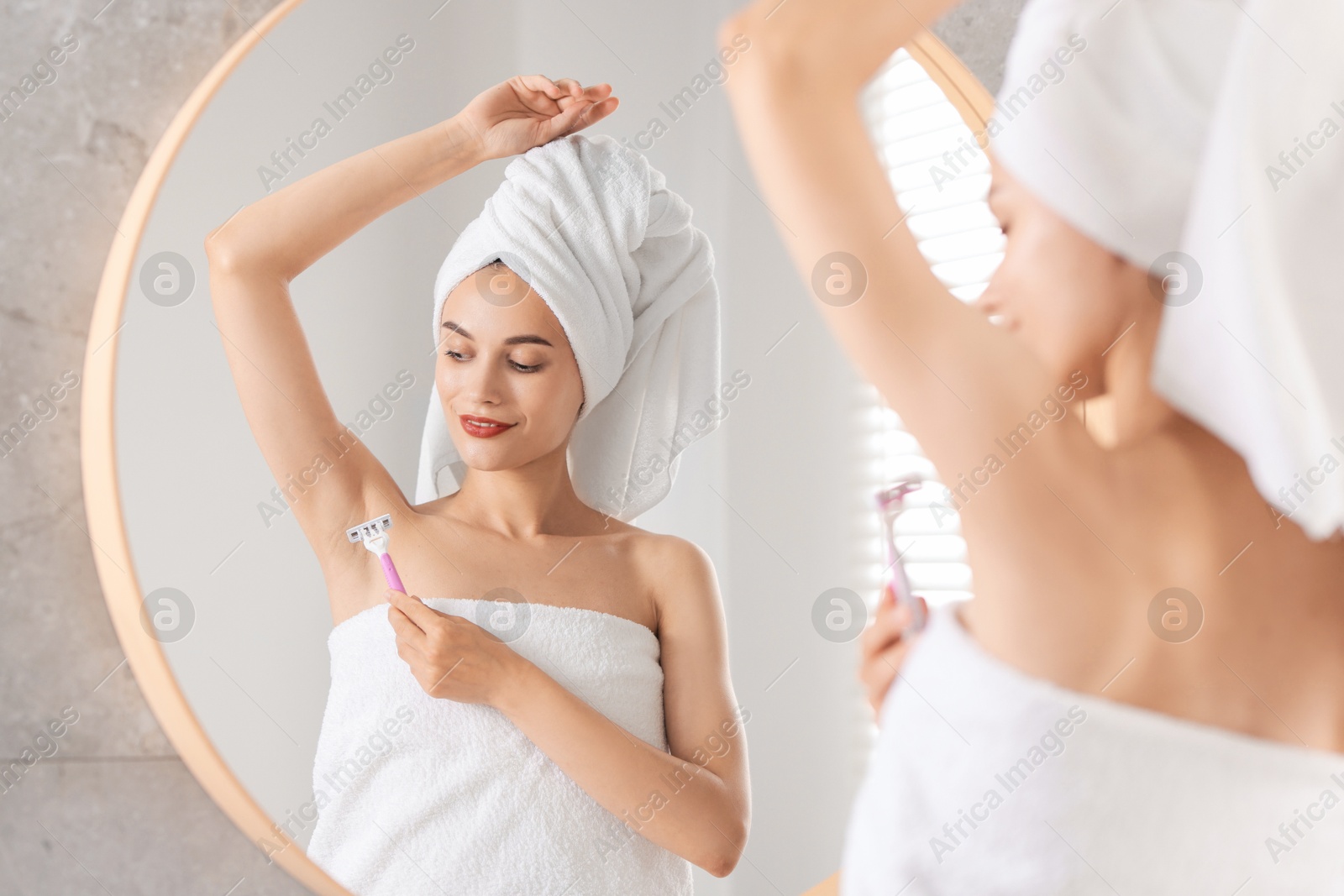 Photo of Smiling woman shaving armpit near mirror indoors, selective focus