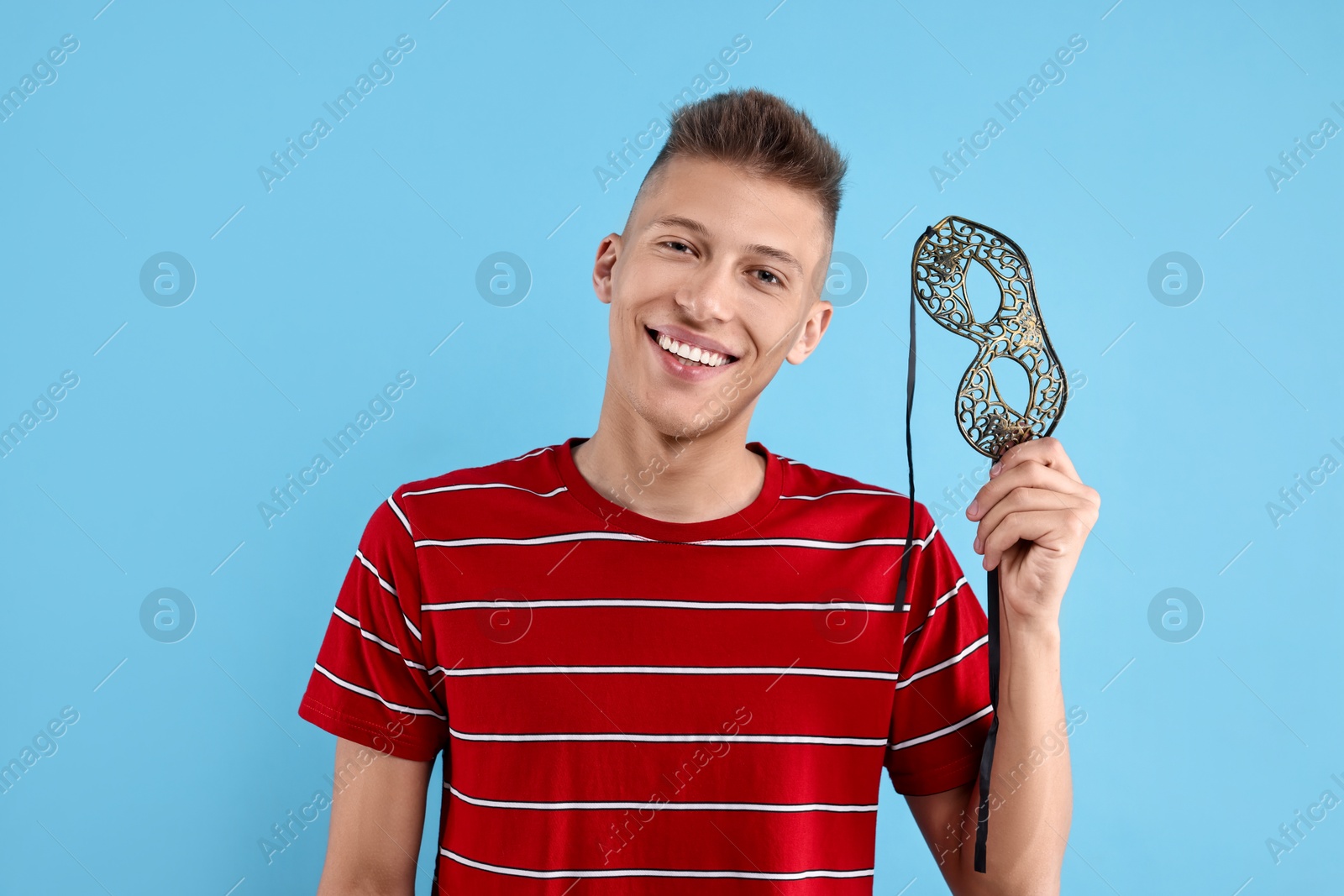 Photo of Charming young man with carnival mask on light blue background