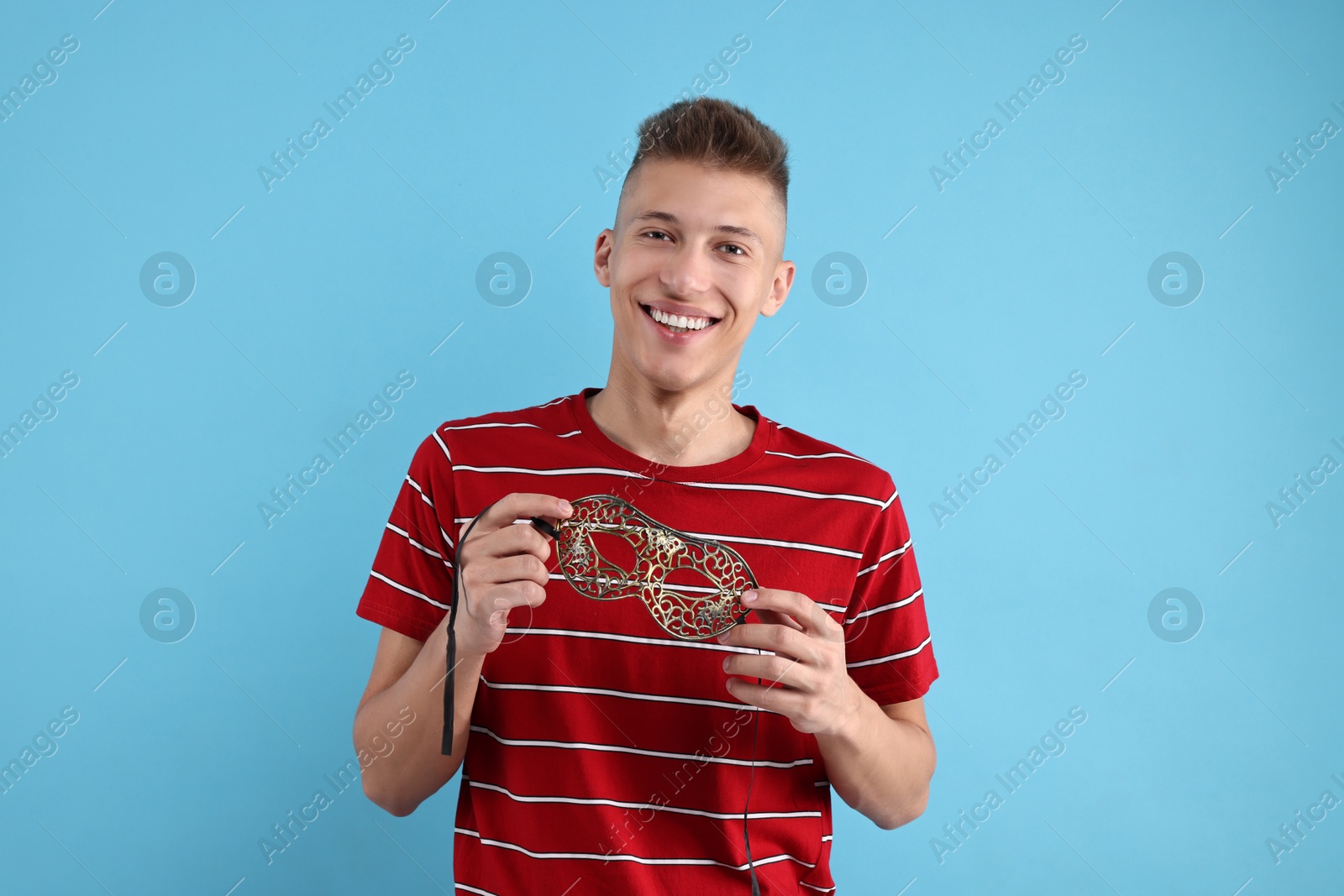 Photo of Charming young man with carnival mask on light blue background