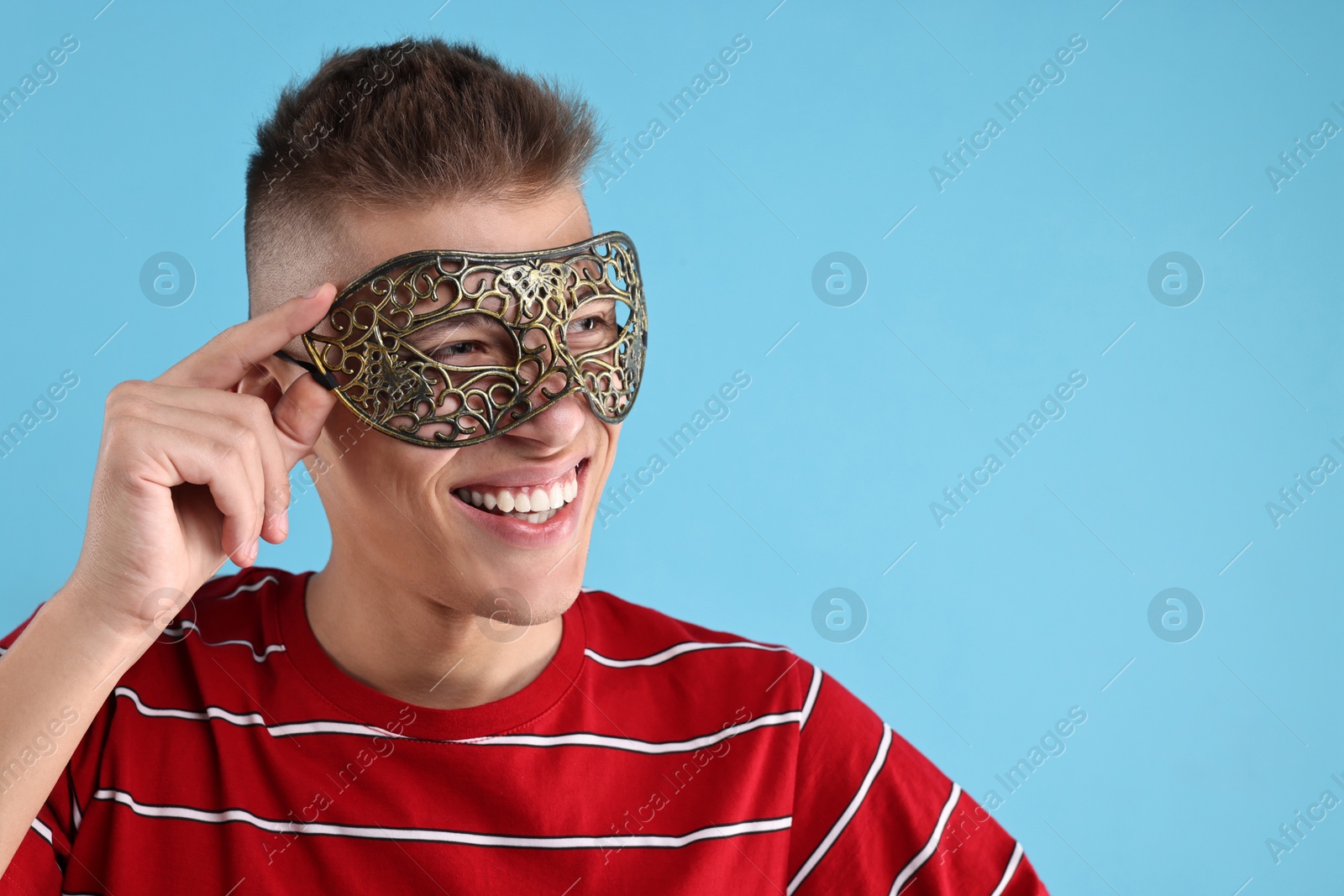 Photo of Charming young man wearing carnival mask on light blue background