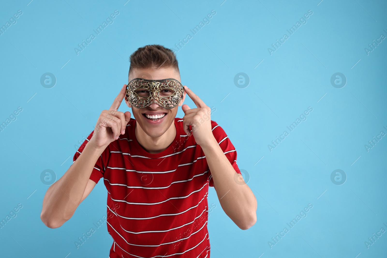 Photo of Charming young man wearing carnival mask on light blue background. Space for text