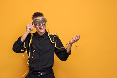 Photo of Charming young man wearing carnival mask on orange background. Space for text