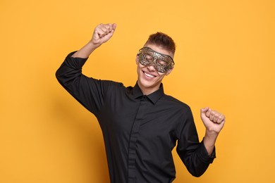 Charming young man wearing carnival mask on orange background