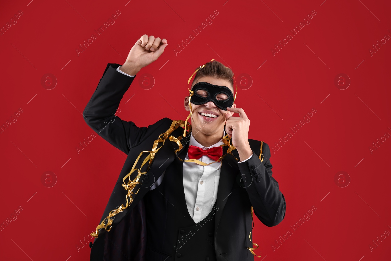 Photo of Charming young man wearing carnival mask on red background