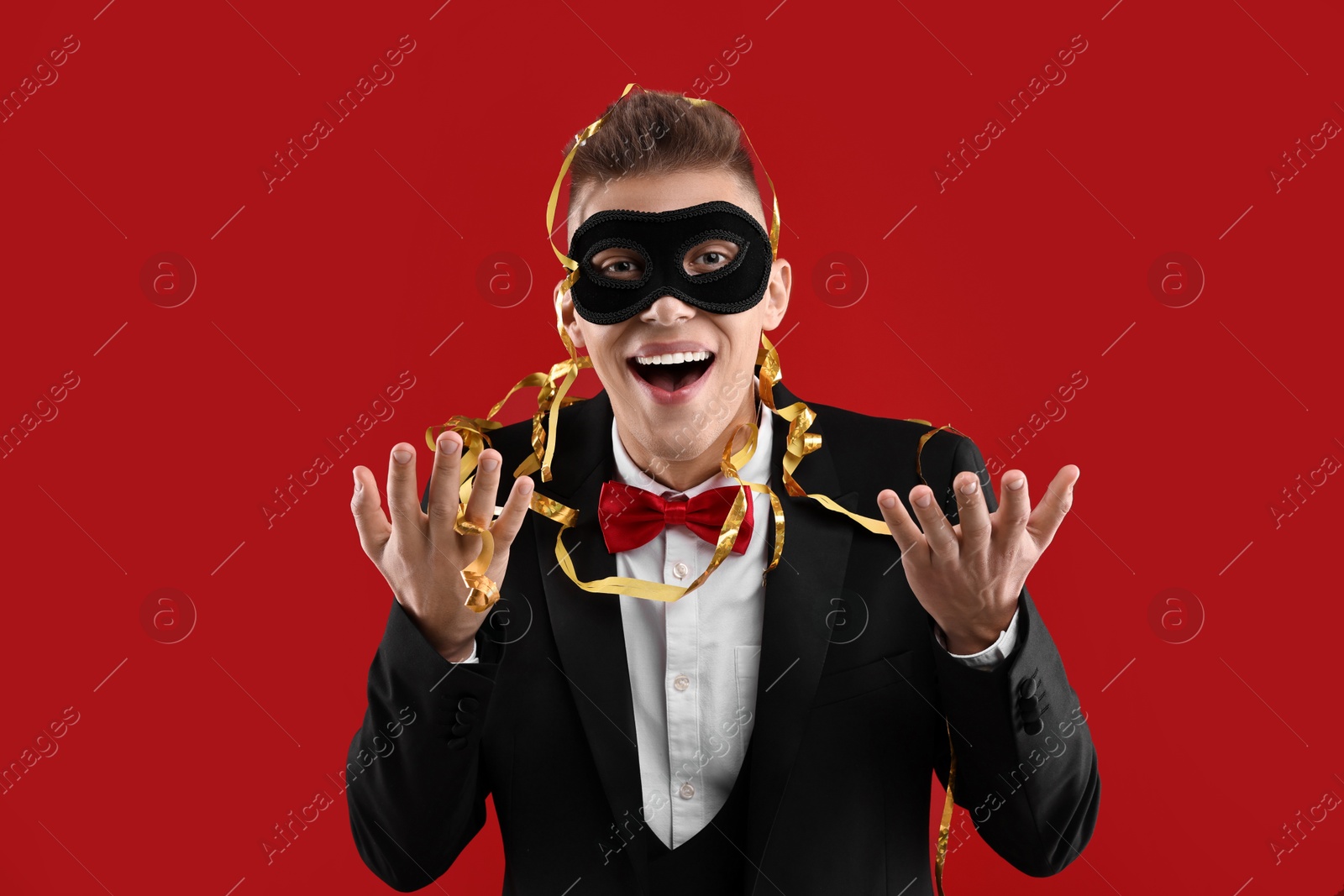 Photo of Charming young man wearing carnival mask on red background