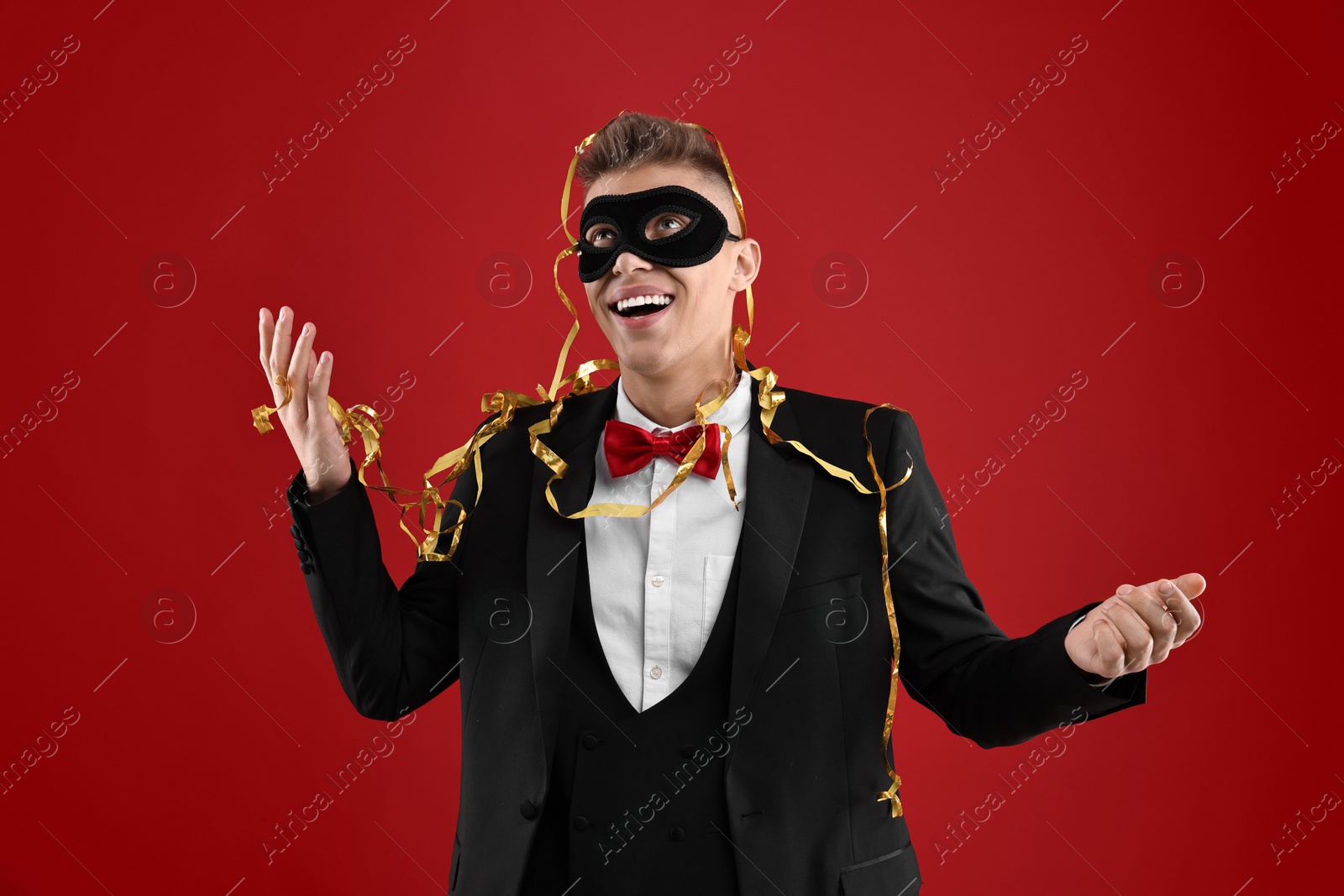 Photo of Charming young man wearing carnival mask on red background