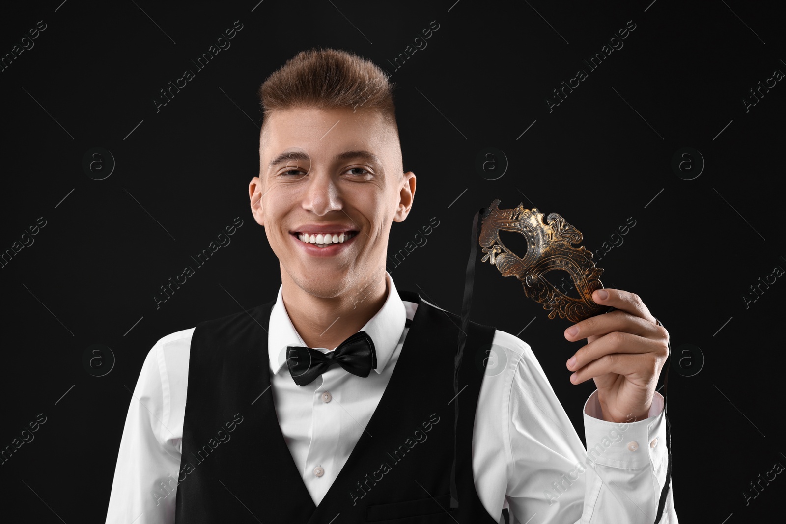 Photo of Charming young man with carnival mask on black background