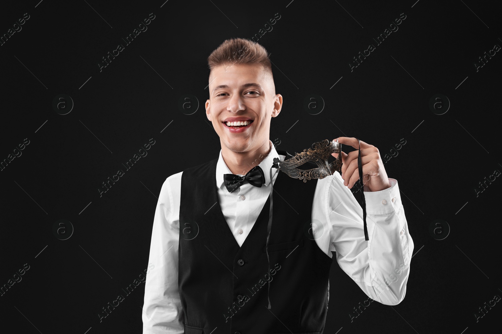 Photo of Charming young man with carnival mask on black background