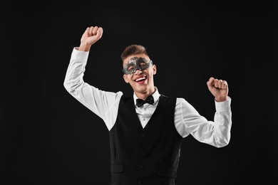 Charming young man wearing carnival mask on black background