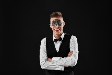 Charming young man wearing carnival mask on black background