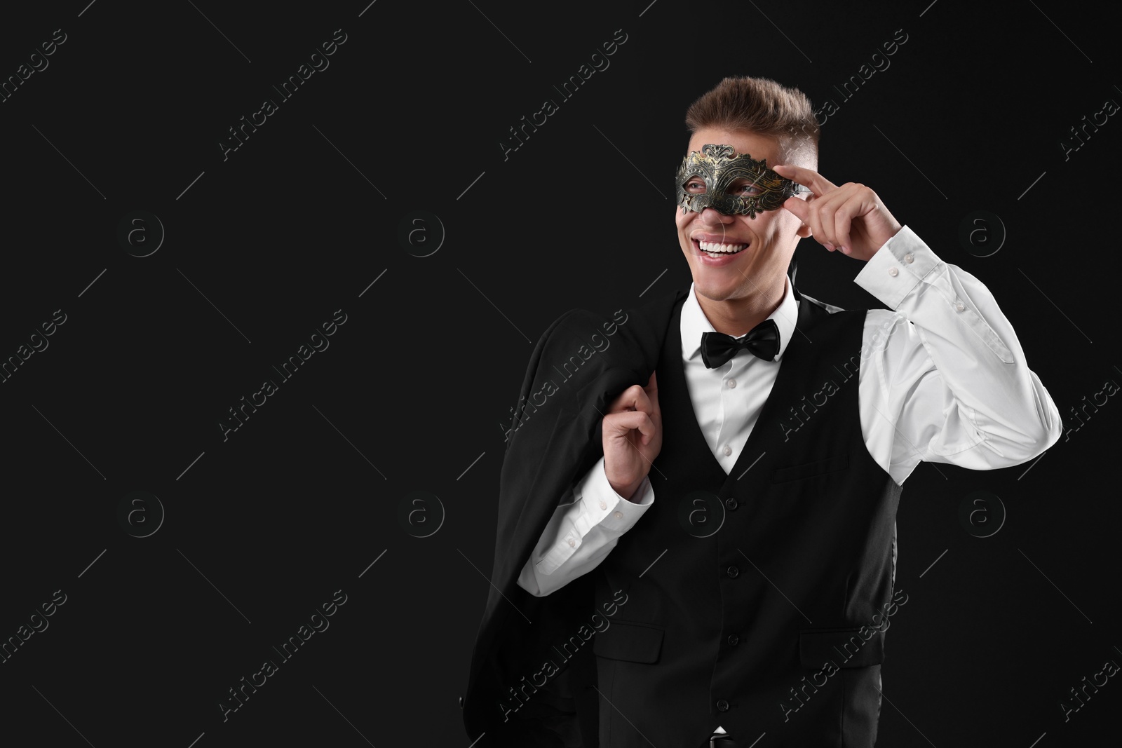 Photo of Charming young man wearing carnival mask on black background. Space for text