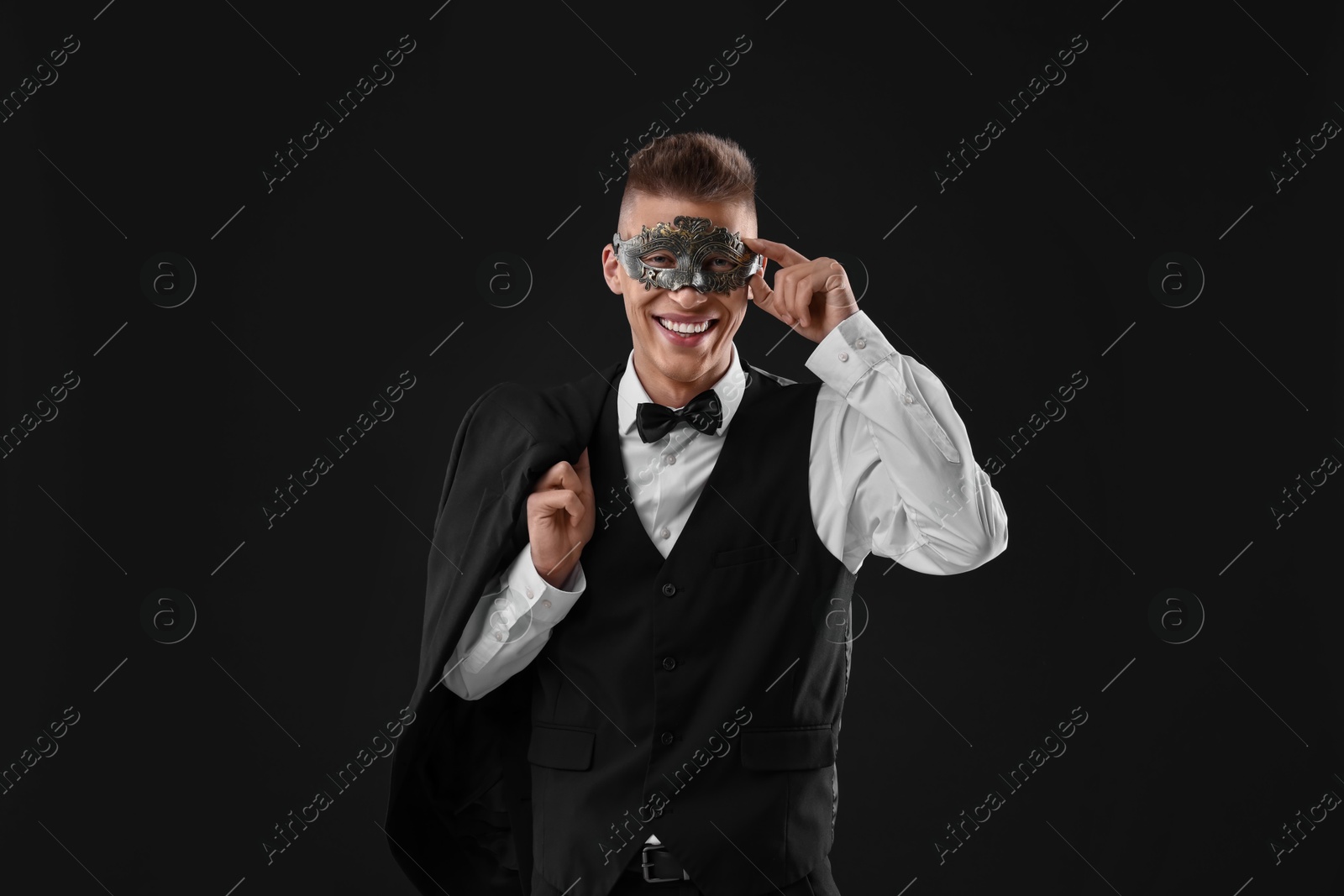 Photo of Charming young man wearing carnival mask on black background