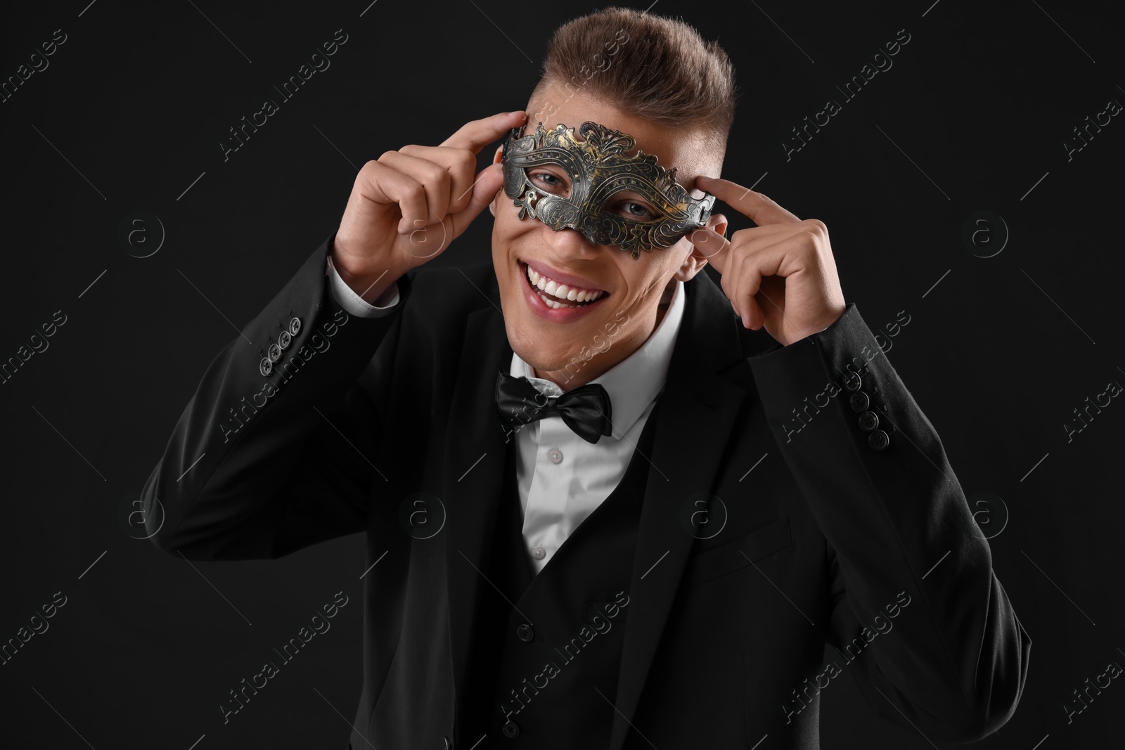 Photo of Charming young man wearing carnival mask on black background