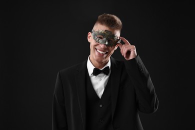 Photo of Charming young man wearing carnival mask on black background