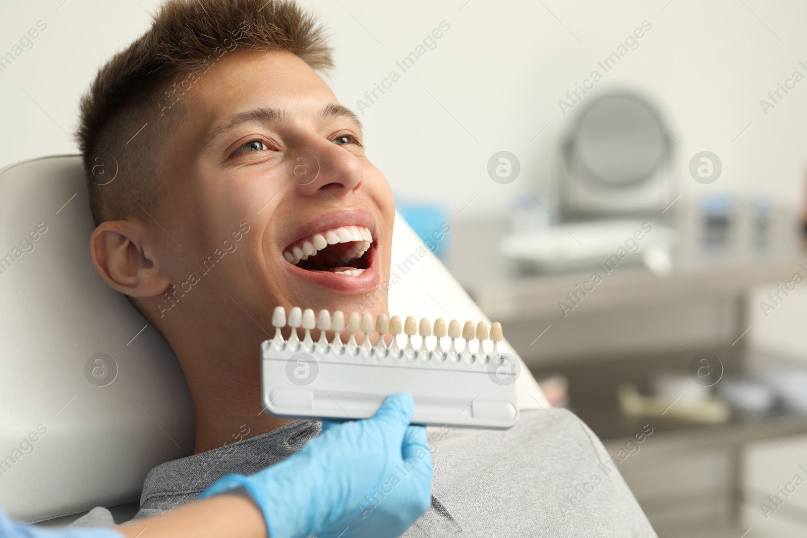 Photo of Doctor checking young man's teeth color in clinic, closeup. Dental veneers