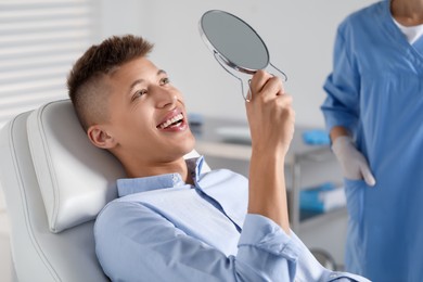 Happy young man with mirror in clinic, closeup. Dental veneers