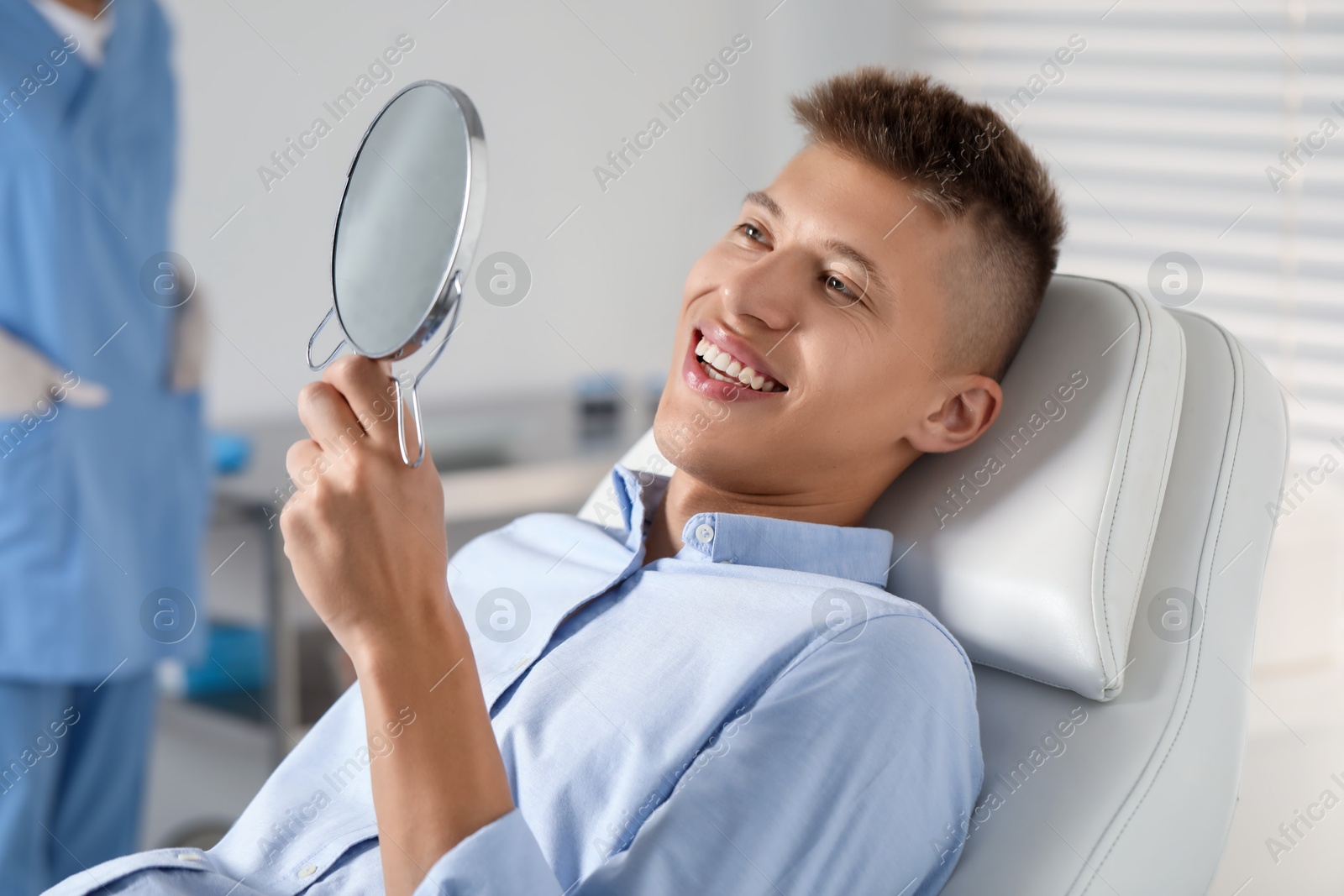 Photo of Happy young man with mirror in clinic, closeup. Dental veneers