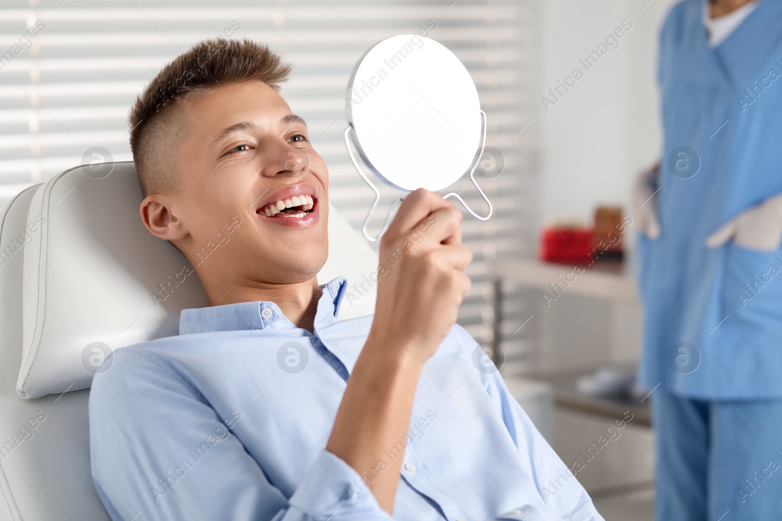 Photo of Happy young man with mirror in clinic, closeup. Dental veneers