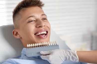 Doctor checking young man's teeth color in clinic, closeup. Dental veneers