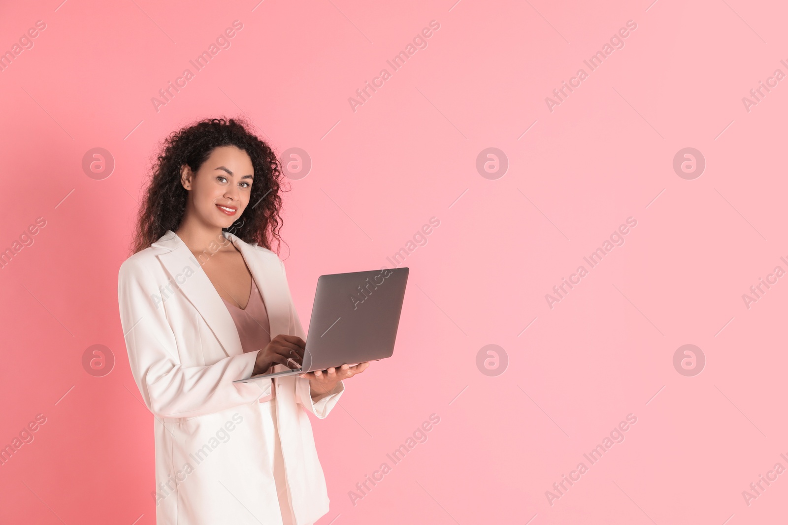 Photo of Beautiful woman in stylish jacket with laptop on pink background, space for text