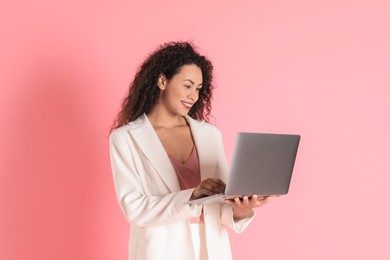 Beautiful woman in stylish jacket with laptop on pink background