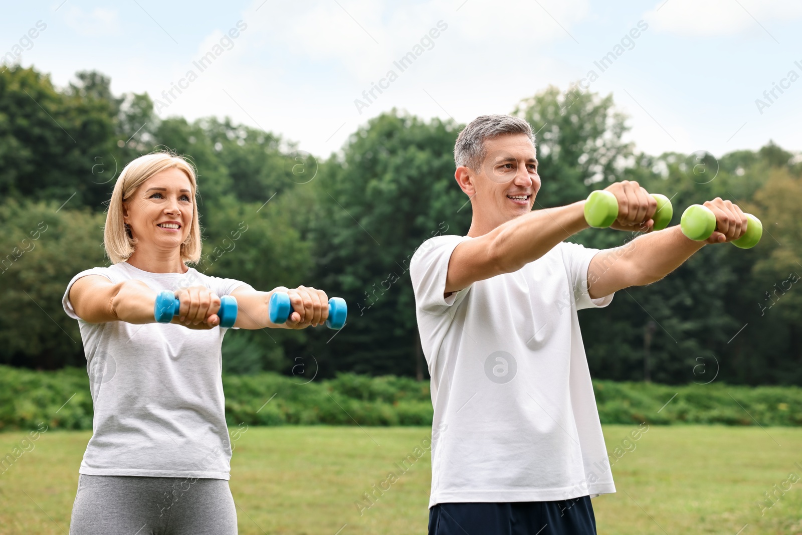 Photo of Happy couple doing exercise with dumbbells in park