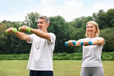 Photo of Happy couple doing exercise with dumbbells in park