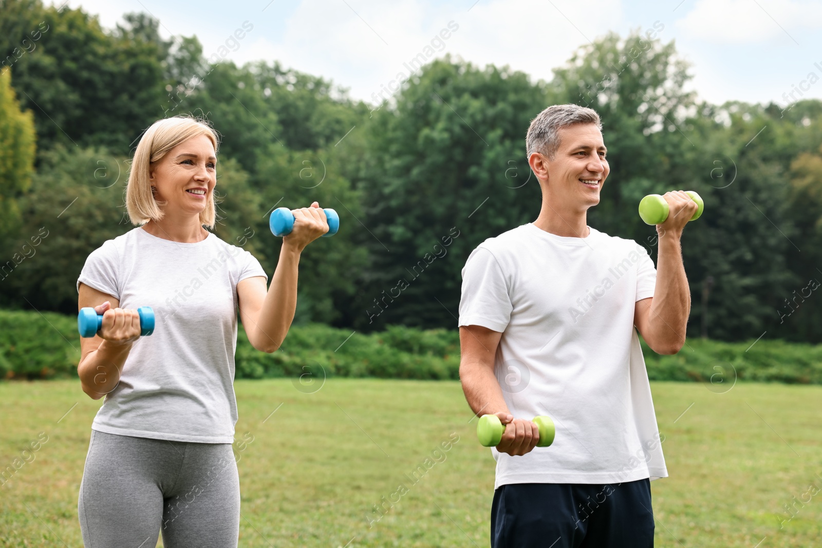 Photo of Happy couple doing exercise with dumbbells in park