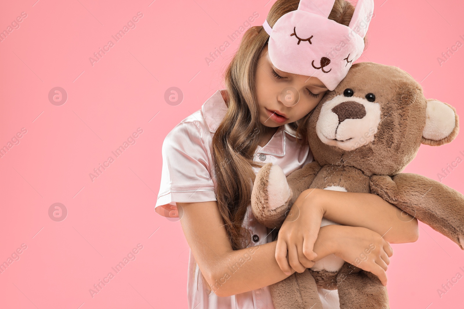 Photo of Overslept girl with sleep mask and teddy bear on pink background, space for text