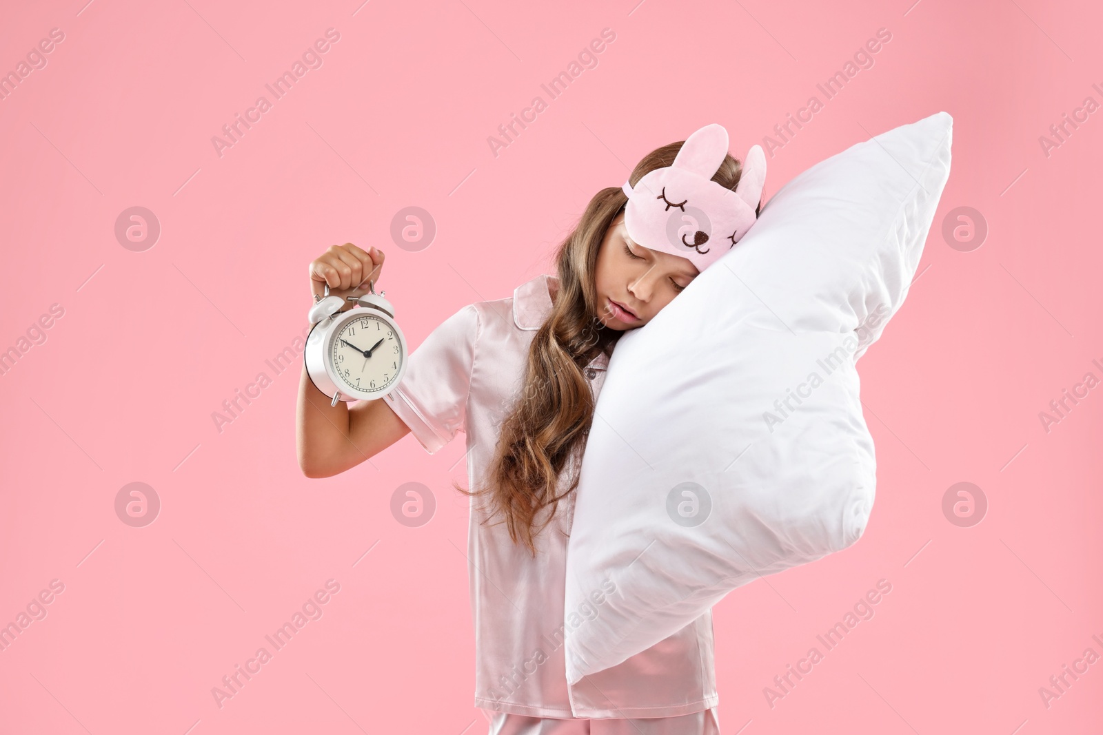 Photo of Overslept girl with sleep mask, pillow and alarm clock on pink background