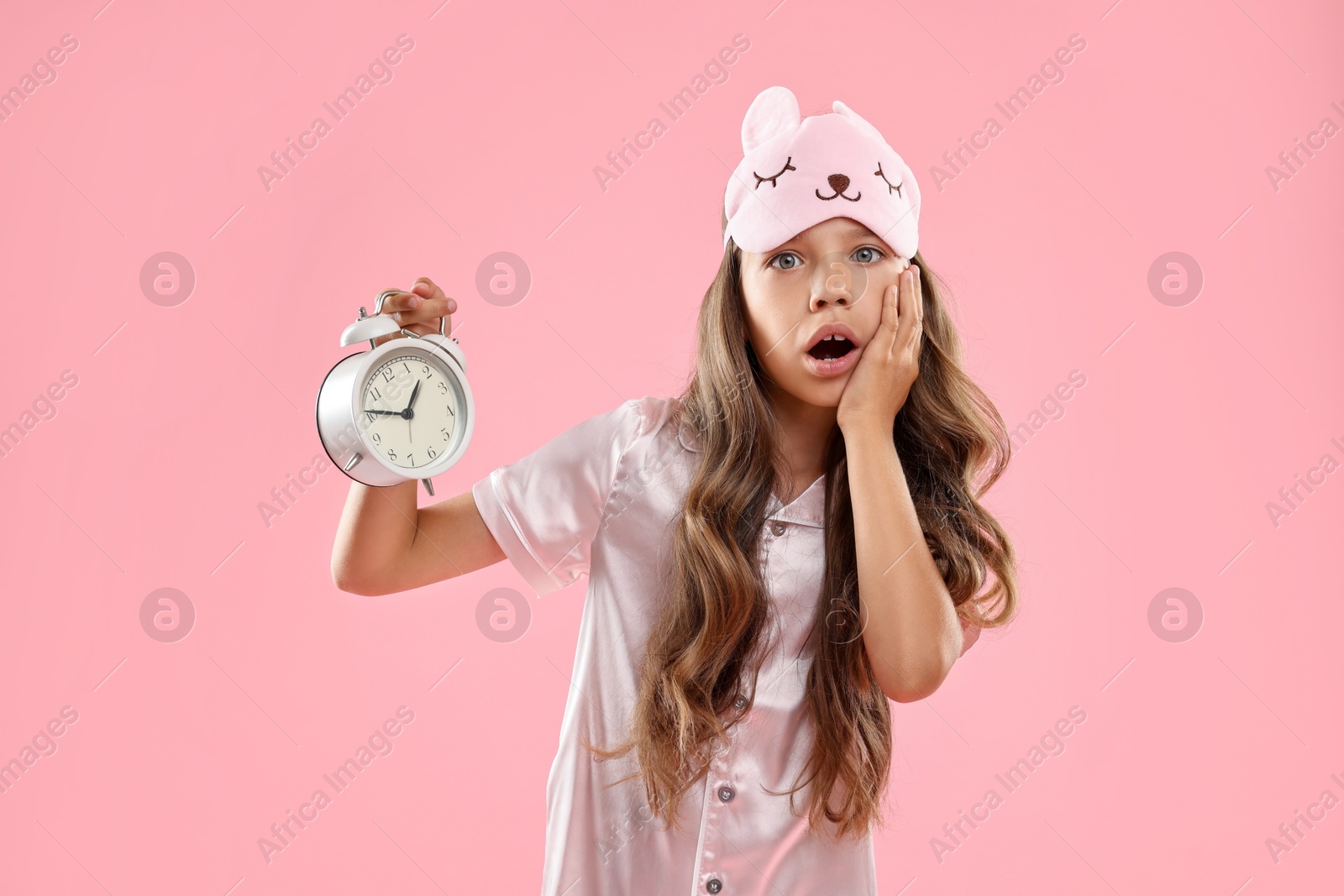 Photo of Overslept girl with sleep mask and alarm clock on pink background